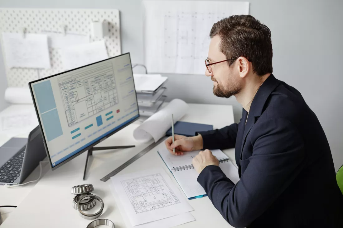 high-angle-portrait-bearded-male-engineer-using-computer-workplace-designing-blueprints-office
